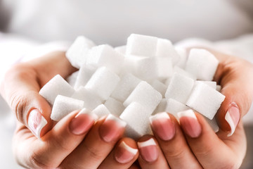 White sugar cubes in woman beautiful hands and perfect nails. Heap of white sugar.