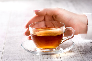 Woman holding a glass cup of black tea. Hot tea in beautiful cup with woman fingers and perfect french nails.