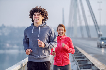 Smiling happy caucasian couple in sportswear running on bridge. Wintertime. Outdoor fitness concept.