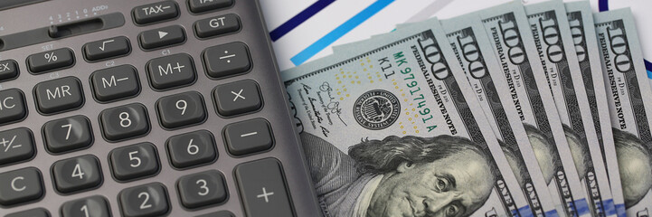 Silver calculator with gray keyboard is lying on desk cash dollar plots in home office setting. Calculation of family expenses social income population freelance irs situation growth research concept