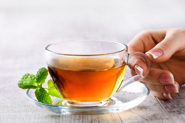 Woman holding a cup of hot green tea in nice glass cup. Green tea on white table with mint leaf.
