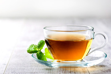 Green hot  tea in clear glass cup on white table. Fresh tea with mint leaf.