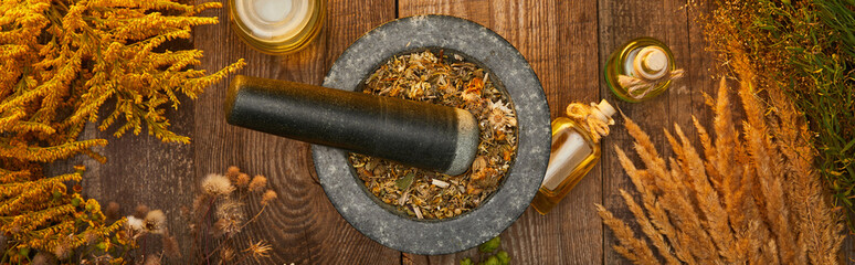 panoramic shot of mortar and pestle dry herbal blend near bottles on wooden table