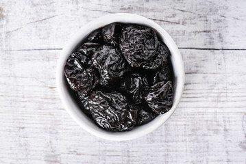 Prunes in white ceramic bowl on white rustic table. Dried plums on white table.