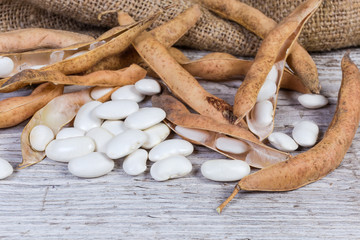 Dry pods, husked kidney beans on wooden surface with sackcloth