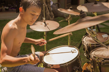 Asian American teenager playing drums. Summer portrait of handsome young boy practicing on drum kit at home garden rehearsing rock song enjoying his hobby