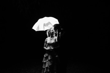 silhouette of a bride and groom under an umbrella on their wedding day.  It is night time and the umbrella is illuminated.