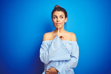 Young beautiful woman wearing bun hairstyle over blue isolated background Thinking concentrated about doubt with finger on chin and looking up wondering