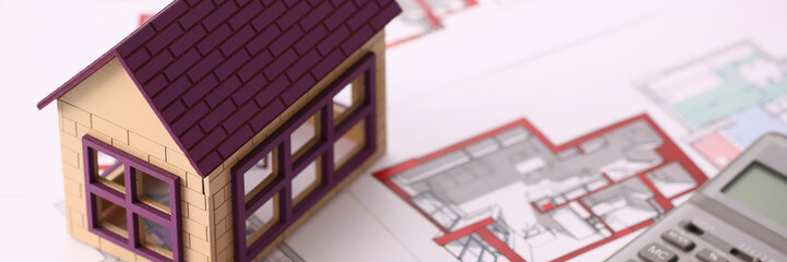 Small miniature house stands on drawing and calculator table in office. Dream of a suburban housing mortgage loan credit concept