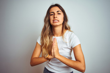 Fototapeta premium Young beautiful woman wearing casual white t-shirt over isolated background begging and praying with hands together with hope expression on face very emotional and worried. Asking for forgiveness