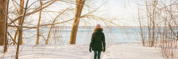 Winter forest walk active woman walking in snow trail outdoor nature panoramic banner. Healthy lifestyle outdoors leisure activity panorama.