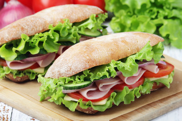Two sandwiches with fresh vegetables, ham and cheese in ciabatta bread	