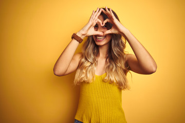 Young beautiful woman wearing t-shirt over yellow isolated background Doing heart shape with hand...
