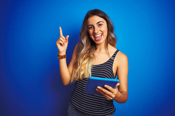 Fototapeta premium Young beautiful woman using touchpad tablet over blue isolated background very happy pointing with hand and finger to the side