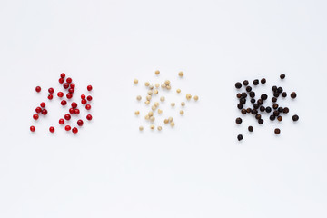 Red, white and black peppercorns on white