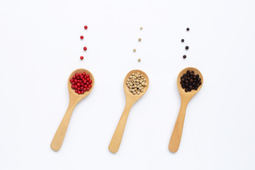 Red, white and black peppercorns with wooden spoon on white.