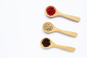 Red, white and black peppercorns with wooden spoon on white.