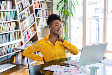 Portrait of young black stressed woman sitting at home office desk in front of laptop, touching...