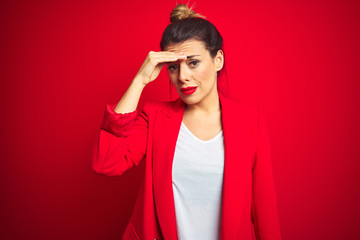Young beautiful business woman standing over red isolated background worried and stressed about a problem with hand on forehead, nervous and anxious for crisis