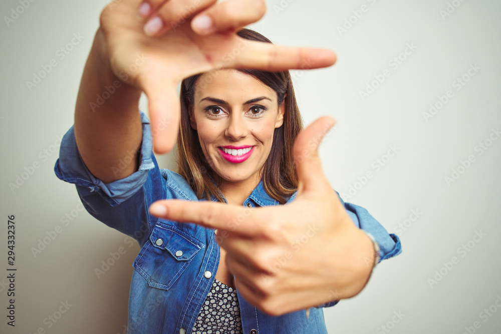 Sticker Young beautiful woman standing over isolated background smiling making frame with hands and fingers with happy face. Creativity and photography concept.