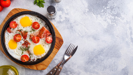 Fried eggs with bacon and tomatoes on a frying pan. Top view. Space for text