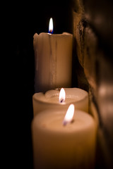 Background or texture of large white burning candles in dark room near brick wall. Holiday. Helloween.