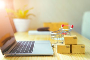 Brown paper boxs and a shopping cart with laptop keyboard on wood table in office background.Easy shopping with finger tips for consumers.Online shopping and delivery service concept.