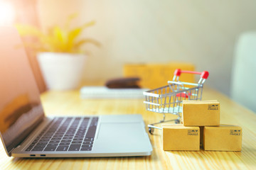 Brown paper boxs and a shopping cart with laptop keyboard on wood table in office background.Easy...