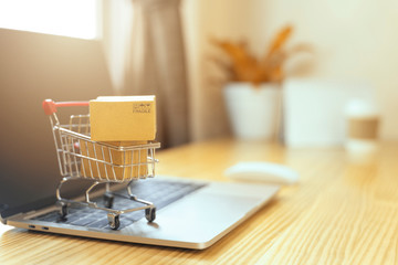 Brown paper boxs in a shopping cart with laptop keyboard on wood table in office background.Easy...