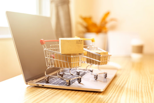 Brown paper boxs in a shopping cart with laptop keyboard on wood table in office background.Easy shopping with finger tips for consumers.Online shopping and delivery service concept.