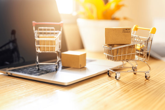 Brown paper boxs in a shopping cart with laptop keyboard on wood table in office background.Easy shopping with finger tips for consumers.Online shopping and delivery service concept.