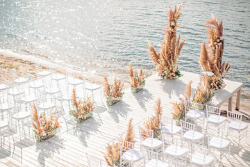 Wedding by the river. Beach wedding venue. Wooden stage with floral decorations arch