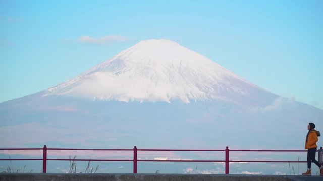 Asian woman wearing yellow jacket walking on the hill with background of Mt. Fuji. Concept of traveling to Japan.