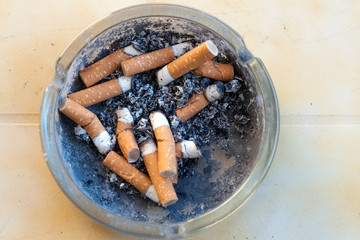 Many cigarette stubs and ash in a glass ashtray on a table