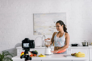 selective focus of happy blogger near blender with tasty smoothie and digital camera