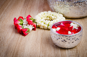 Water in water dipper with colorful flowers pedestal On an old wood background for Songkran festival, Thailand,