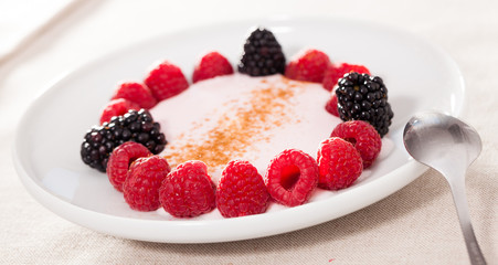 raspberries and blackberries laid out on a white plate in circle with yogurt and cinnamon