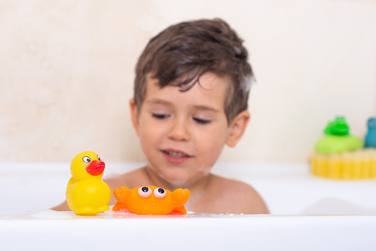 Hygiene for infant and baby. Child playing with soap foam in home bathroom. Rubber duck in foam bath