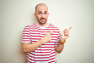 Fototapeta premium Young bald man with beard wearing casual striped red t-shirt over white isolated background Pointing aside worried and nervous with both hands, concerned and surprised expression
