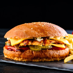 Burgers with juicy cutlet, fresh vegetables, crispy bun with sesame seeds on a wooden table. Traditional fast food.