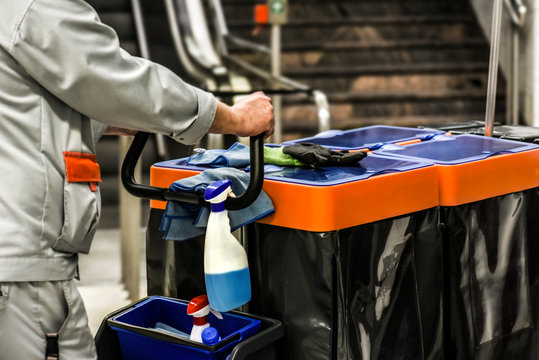 Industrial cleaner with big bags of garbage and clean spray hanging on hand holders. Charman push handcart with clean product and waste.