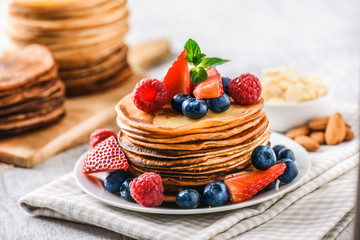 Pancakes with forest fruits berries on white table. Fresh pancakes on cloath with almonds. Blueberries, raspberries on pancakes.