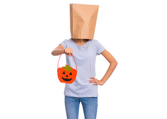 Happy halloween concept. Teen girl with paper bag over her head holds orange pumpkin bucket, isolated on white background. Portrait of teenager cover head with bag. Child waiting candy.
