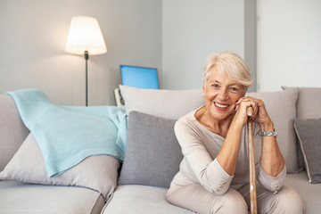Smiling grandmother sitting on couch. Portrait of a beautiful smiling senior woman with walking...