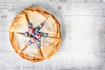 Top view of fresh delicious pancakes on white table with white sugar and forest fruits like blueberries, raspberries.