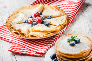 Baked heap of pancakes with blueberries and mint leaf. Pancakes on white table and red square cloth.