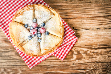 Top view of pancakes on wooden table. Pancakes with forest fruits like a raspberries and blueberries.