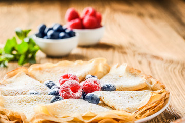 Fresh pancakes on wooden table with forest fruits like a raspberries, blueberries.  Pancakes on plate.