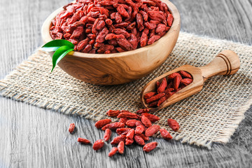 Goji in wooden bowls with green leaves. Goji in scoop. Pile of goji on table.