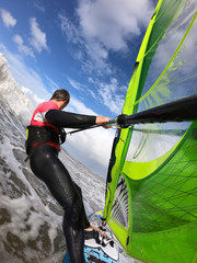 Windsurfing in the wave of the North Sea. Man with windsurfer and wetsuit in sunny weather in front of a wave in the North Sea.